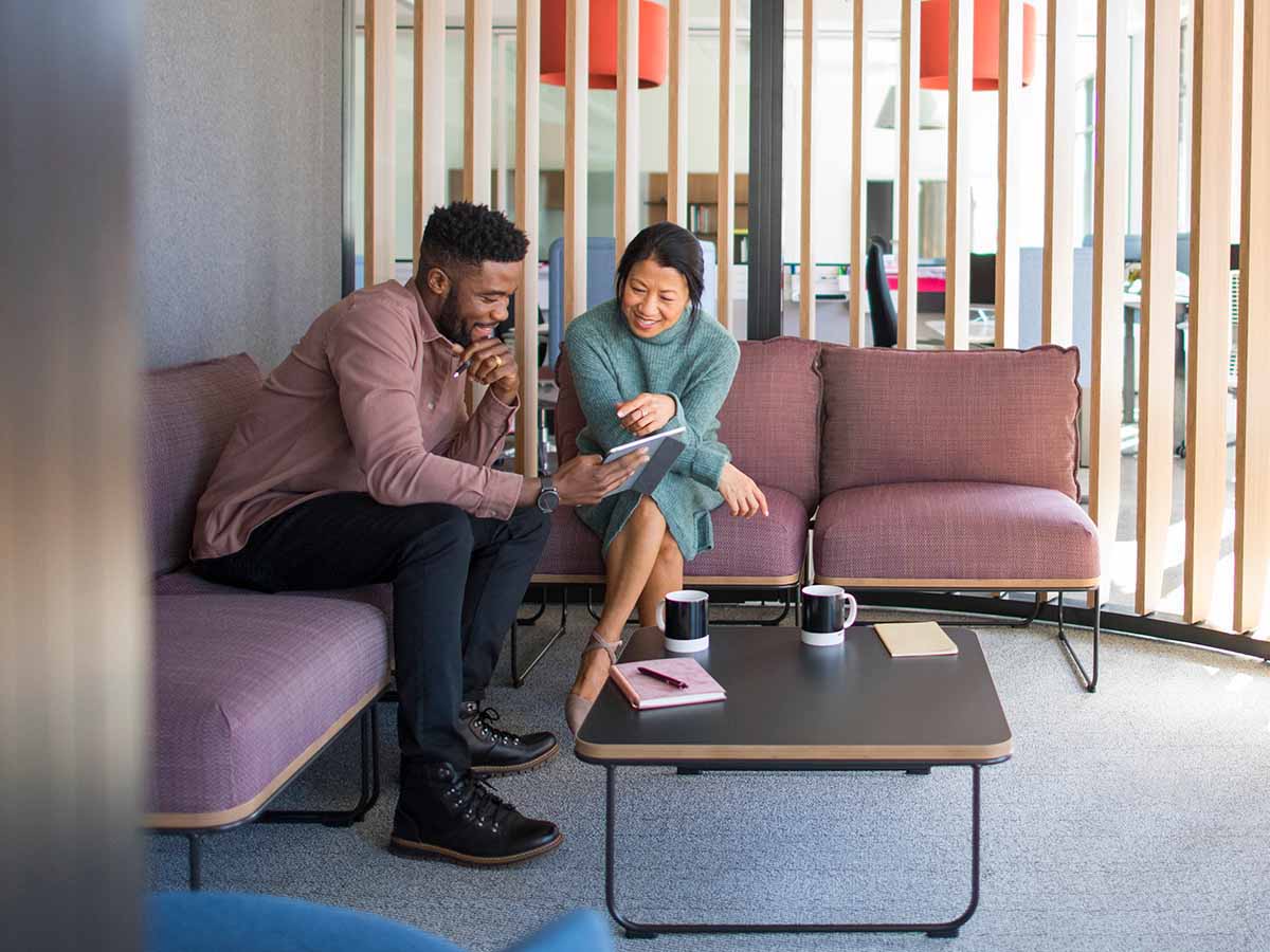 Man and woman conversing together in a seating area while review information on a tablet.