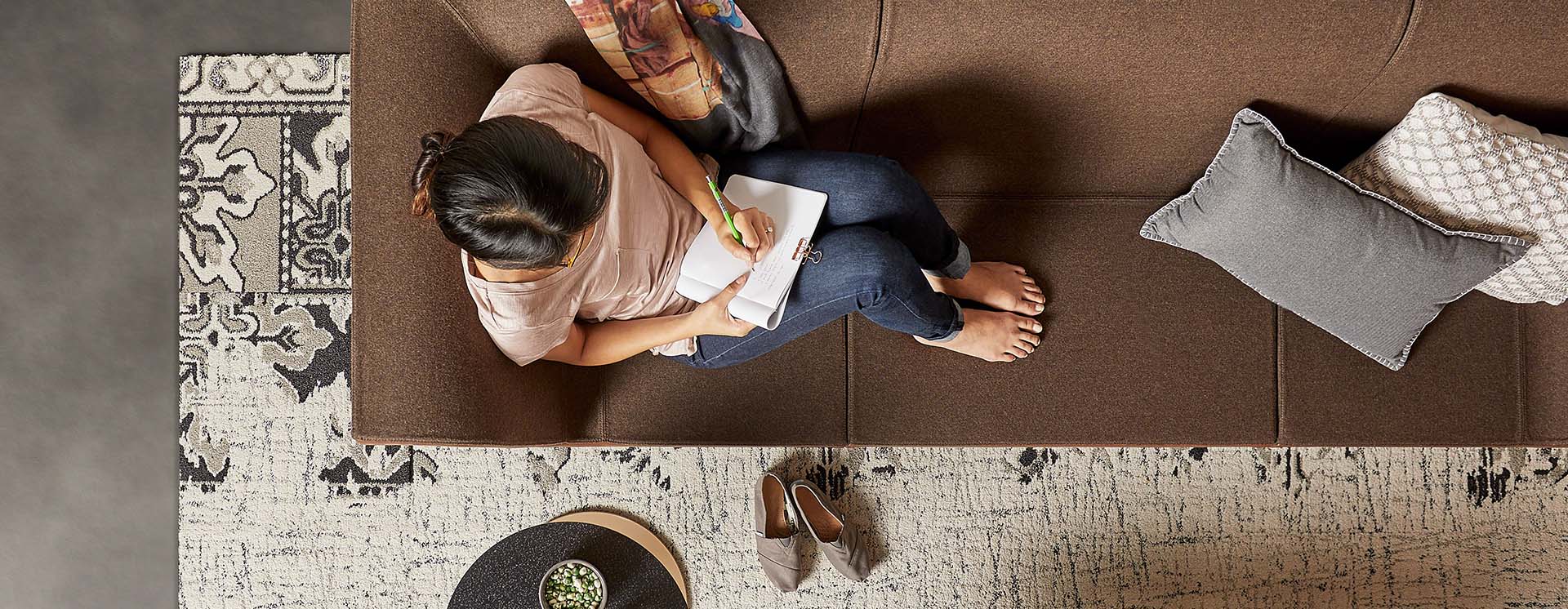 Woman sitting on a brown couch taking notes in a notepad. Shown from above.